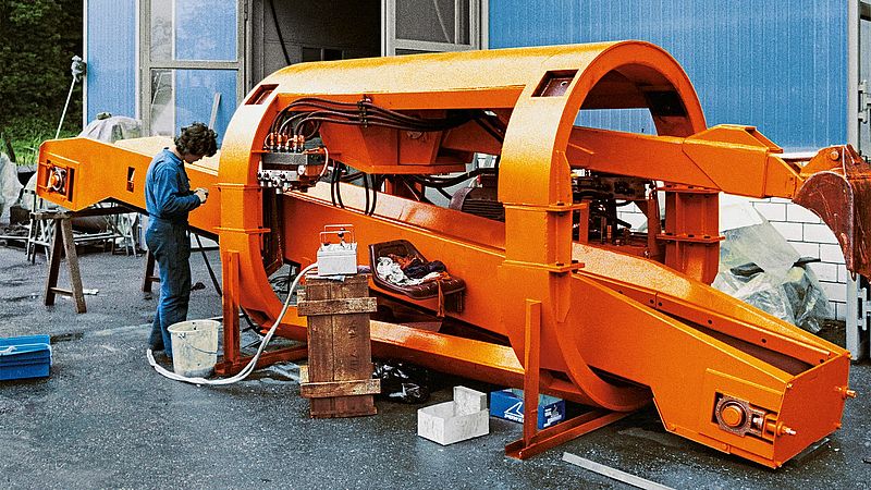 Eine orangene Maschine, an der ein Mitarbeiter arbeitet. 