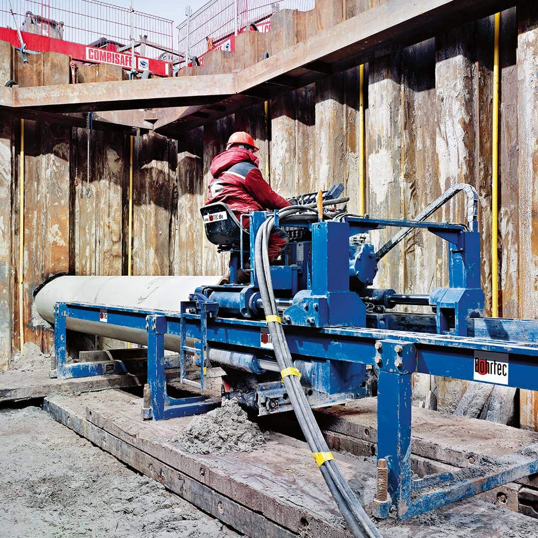 Baustellenmitarbeiter steuert eine blaue Bohrtec Maschine im Boden.   