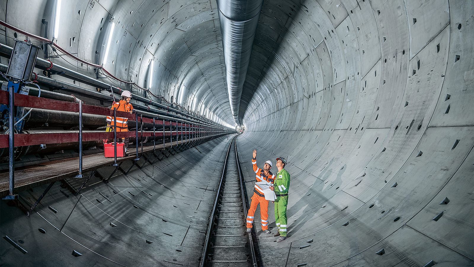 Three construction site workers stand in a tunnel tube and discuss.