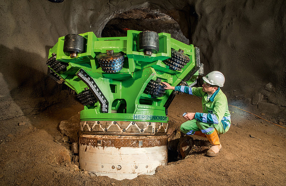Фотография зеленого расширителя на буровой установке перед входом в шахту с рабочим на стройке рядом с ним