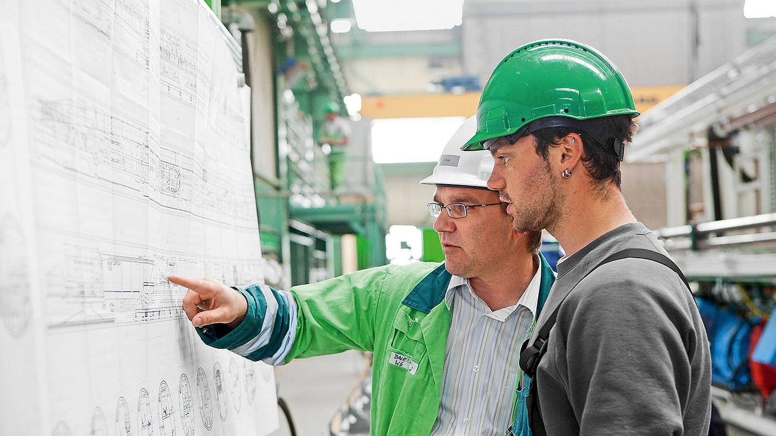 A Herrenknecht employee explains something to another employee and points to the project plan